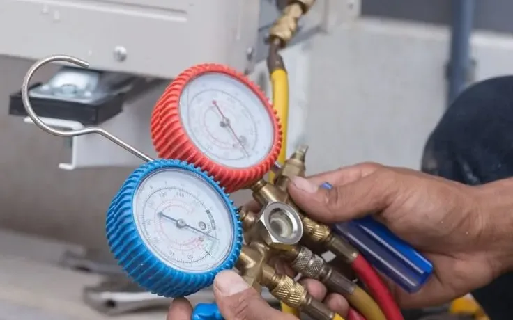 En tekniker holder et manometer for å sjekke trykket på en utendørs klimaanleggsenhet.